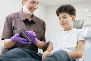 Female pediatric dentist use tablet computer for showing dental results to happy male child in...