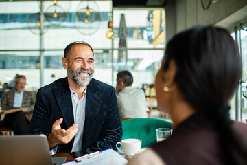 Mature man and adult woman smiling during business meeting at cafe