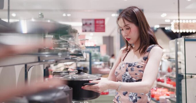Young asian woman holding and examining a premium black cooking pot while shopping for new kitchenware and household equipment in a modern lifestyle shopping mall.