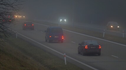 Car traveling on the foggy road with headlights or headlamps on. Low visibility - Dangerous driving...