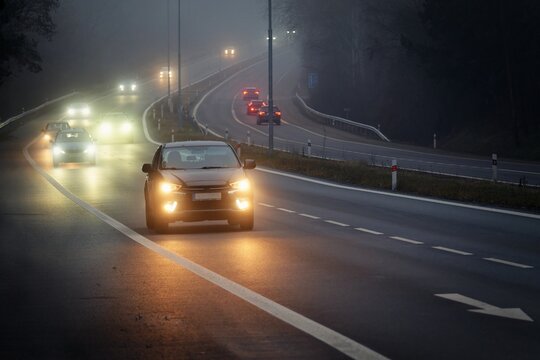 Car traveling on the foggy road with headlights or headlamps on. Low visibility - Dangerous driving of cars in winter in bad weather