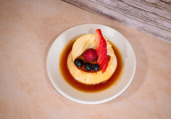 Imagen horizontal de un plato blanco de flan napolitano con caramelo y frutos rojos 