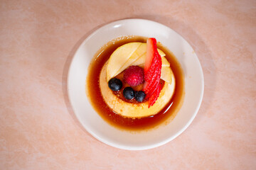 Imagen cenital de un platillo con flan napolitano con caramelo y frutos rojos