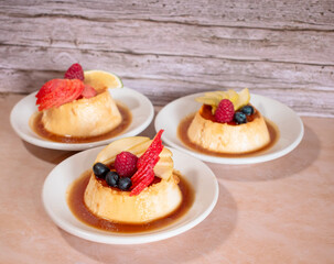 Tres platos de flan con caramelo y decorado con peque&ntilde;os frutos rojos en una mesa de madera