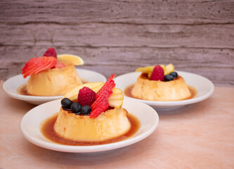 Imagen hoizontal de tres platillos de flan con frutos rojos en fondo de madera
