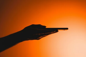 A hand holds a smartphone in front of a vibrant orange sunset background