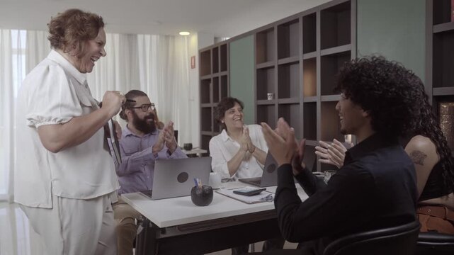 Diverse team of professionals celebrating successful project completion in a modern office environment, clapping and laughing together.