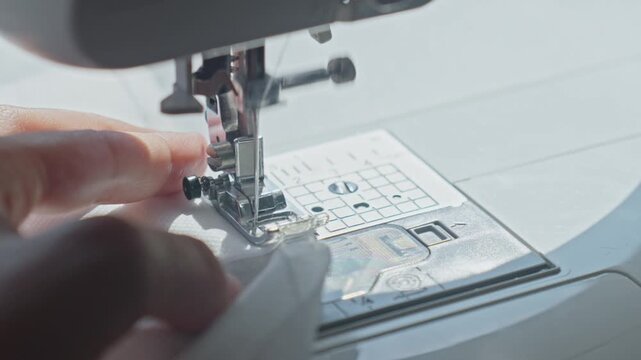 Close up of sewing machine needle stitching white fabric with hands guiding. Concepts of tailoring and textile work