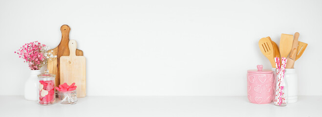 Valentines Day love and heart theme kitchen decor, bakeware and accessories on a white shelf against a white wall. Copy space.