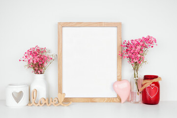 Mock up wood frame with Valentines Day decor and flowers. White shelf against a white wall. Copy space.