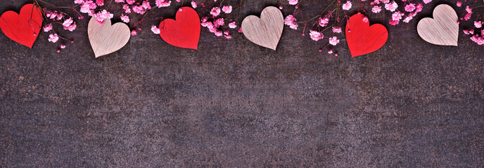 Valentines Day top border of wooden hearts and pink flowers. Overhead view on a dark banner background. Copy space.