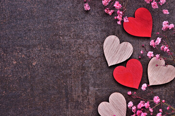 Valentines Day side border of wooden hearts and pink flowers. Top view on a dark background. Copy space.