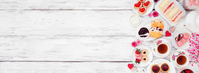 Valentines Day or love theme afternoon tea. Top down view side border against a white wood banner background. Assortment of finger sandwiches, sweet desserts and pastries. Copy space.