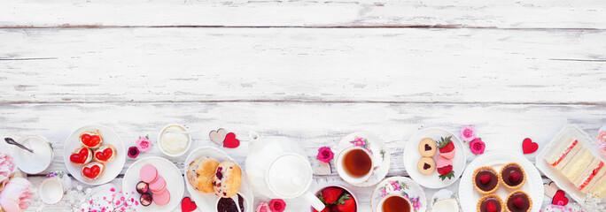Valentines Day or love theme afternoon tea. Top down view bottom border against a white wood banner background. Variety of finger sandwiches, sweet desserts and pastries. Copy space.