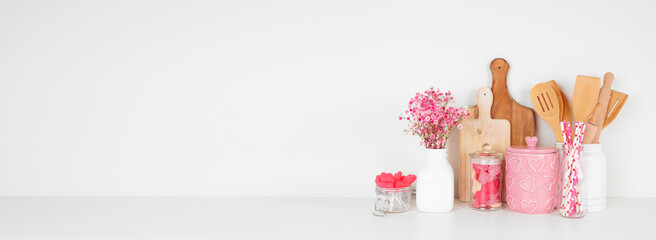 Valentines Day love and heart theme kitchen decor, bakeware and accessories on a white shelf against a white wall. Copy space.