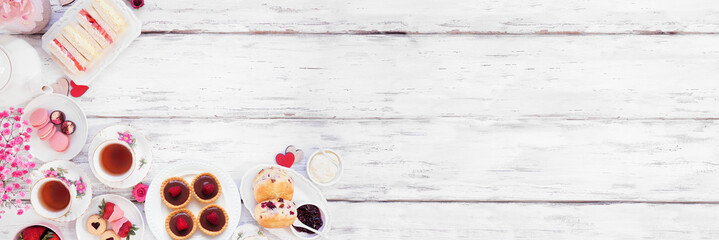 Valentines Day or love theme afternoon tea. Overhead view corner border against a white wood banner background. Assortment of finger sandwiches, sweet desserts and pastries. Copy space.
