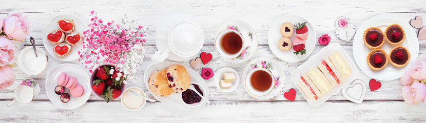 Valentines Day or love theme afternoon tea. Top view table scene against a white wood banner background. Assortment of finger sandwiches, sweet desserts and pastries.
