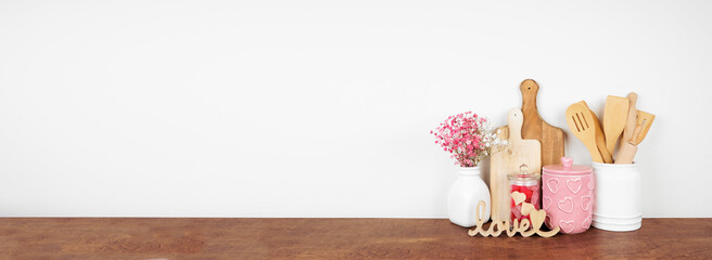 Valentines Day love and heart theme kitchen decor, bakeware and accessories on a wooden shelf against a white wall. Copy space.