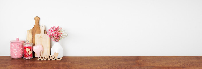 Valentines Day love and heart theme kitchen decor, bakeware and accessories on a wooden shelf against a white wall. Copy space.