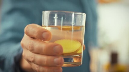 In well-lit kitchen, man extends his hand, presenting transparent glass filled with water slices of fresh ginger, symbolizing natural and invigorating morning ritual that promotes vigor and well-being