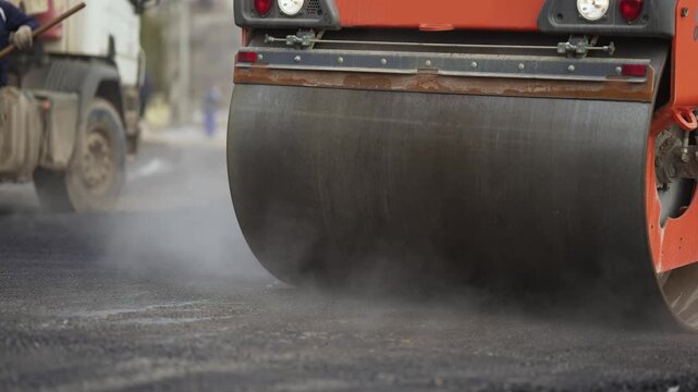 Steam road roller compacting new asphalt on road construction site, slow motion