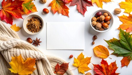 Fall flatlay with colorful leaves, nuts, spices, sweater, and blank card on a white surface