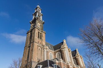 Exterior view of the historic Westerkerk church in Amsterdam, showcasing the tall bell tower and brick architecture against a blue sky.