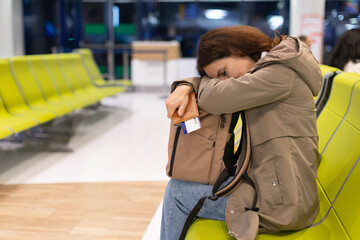 Exhausted adult caucasian woman leaning on backpack while waiting at airport terminal. Travel fatigue and emotional stress lifestyle concept