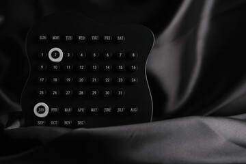 Black perpetual calendar with highlighted January 2nd placed on soft dark fabric, creating dramatic and elegant visual mood.