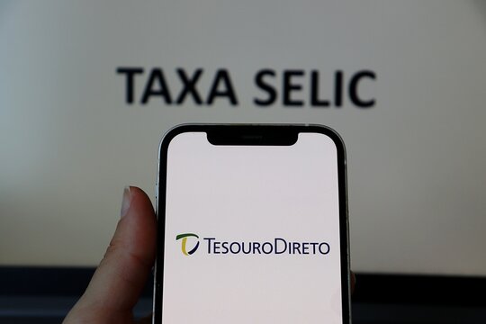 Salvador, Brazil - January 3, 2026: Tesouro Direto logo on a smartphone screen with Taxa Selic text in the background. Brazilian interest rates and public bonds investment concept.