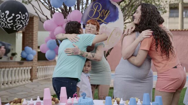 Happy pregnant woman celebrating at a gender reveal party with friends and family in a backyard.