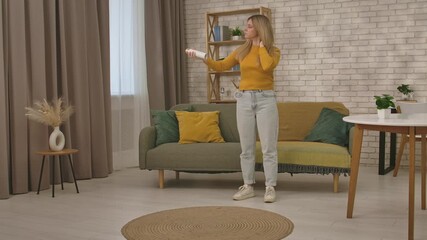 A woman in casual attire sprays her hair in a cozy living room with stylish decor and natural light.