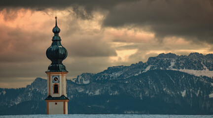 Nahaufnahme eines traditionellen Zwiebelturms in Bayern vor den Alpen. Winterliche Abendstimmung mit dramatischen Wolken im Chiemgau, Oberbayern. © florentina.p