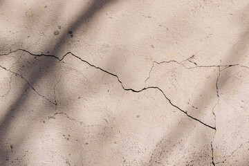 Diagonal shadows on a painted light beige old cracked concrete wall on a sunny day