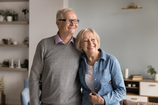 Peaceful dreams of aging together. Serene smiling senior couple loving pensioner age spouses hug in living room look aside enjoy calm harmony of mature love feel confidence in happy retirement future
