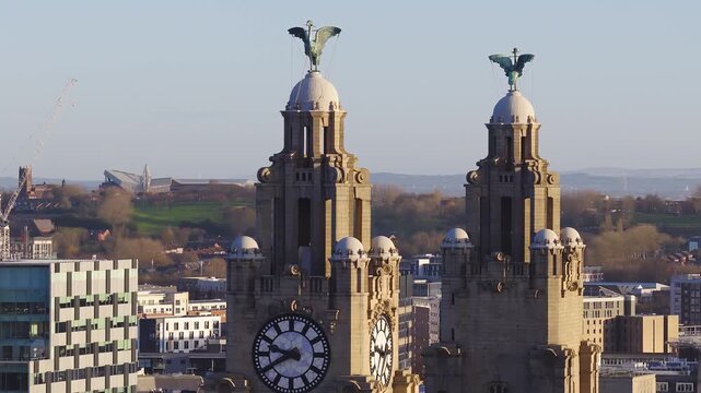 Aerial sunrise focuses on the Royal Liver Building in Liverpool, with twin clock towers, Liver Birds, ornate stonework, and skyline and riverfront appearing.