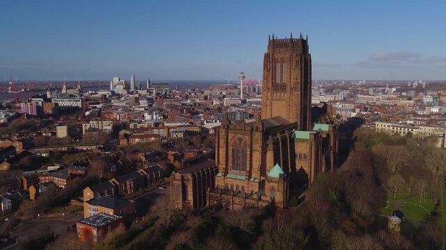 Aerial sunrise shows Liverpool Cathedral, trees, terraces, River Mersey, Ferris wheel, Radio City Tower, and dockland buildings as the drone pans and moves forward.