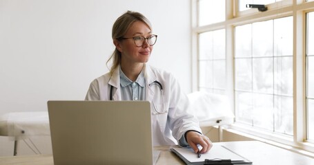 Professional female doctor in white coat and stethoscope working at desk with laptop and clipboard, review patient data, analyze medical records in modern medical office. Healthcare services, workflow - Powered by Adobe