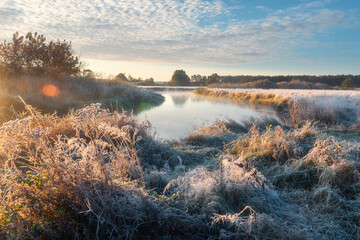 Scenic river landscape on a cold, frosty morning. Golden trees line the misty banks under a bright, sunny sky.