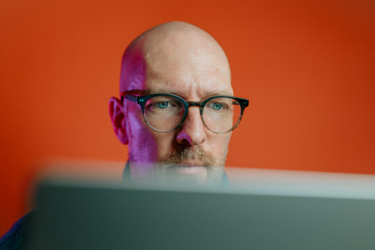 Ein Mann mit Bart in den Vierzigern sitzt am Schreibtisch in seinem B&uuml;ro oder Home-Office und nutzt seinen Laptop f&uuml;r sein Business.