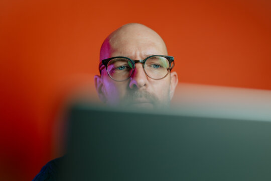 Ein Mann mit Bart in den Vierzigern sitzt am Schreibtisch in seinem B&uuml;ro oder Home-Office und nutzt seinen Laptop f&uuml;r sein Business.