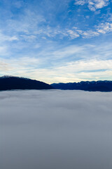 Obraz premium Cloud Sea Over Mountain Ridge at Sunrise: Serene Sky, Mist, and Distant Peaks