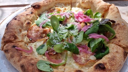Freshly baked pizza with green toppings and pink onions served on a white plate outdoors