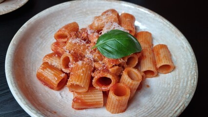 Pasta served on a white plate with basil on top in a restaurant setting during lunch