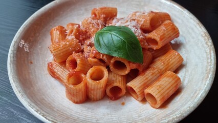 Plate of pasta with tomato sauce and basil on a simple dish in a dining room setting