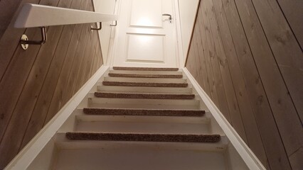 Staircase leading up to a door in a wooden hallway during daytime with soft light illuminating the steps
