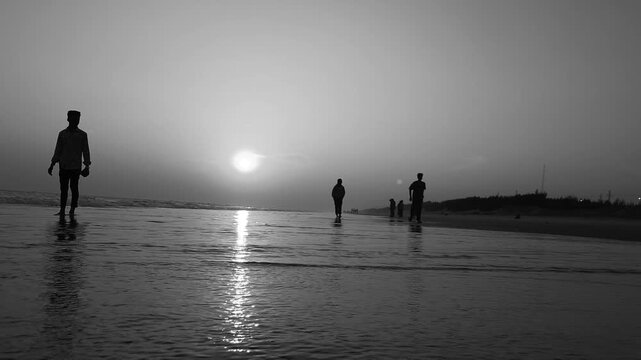 Slow motion footage of kids playing with beach sand at dusk, surrounded by warm glow, fading light, and painted sky, capturing a serene sunset nature and evening sky atmosphere. Black and white