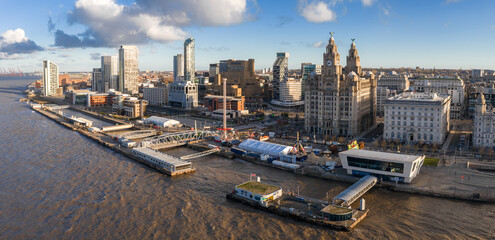Aerial sunrise view of Liverpool along the River Mersey shows the Royal Liver Building, Port of Liverpool, Museum of Liverpool, Albert Dock cranes, and modern high rises.