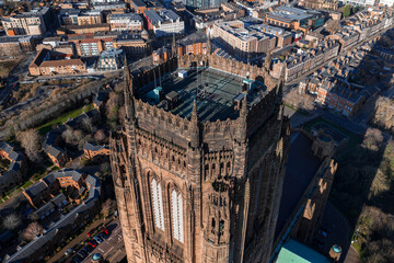 Aerial view of Liverpool Cathedral in Liverpool, UK, shows the sandstone Gothic Revival tower with buttresses and spires at sunrise, long shadows, and nearby urban blocks.