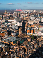 Obraz premium Aerial sunrise view of Liverpool with Radio City Tower left and St Luke's ruins centered. River Mersey, port cranes, wind turbines, St George's Hall, and modern blocks appear.